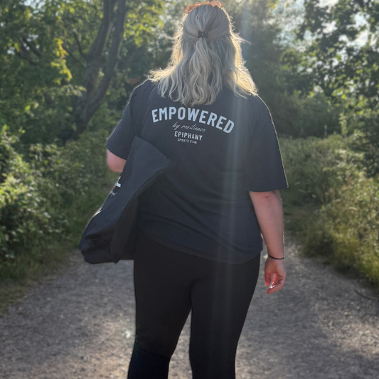 Woman wearing an oversized Empowered T-shirt with leggings, walking on a sunny path surrounded by greenery.